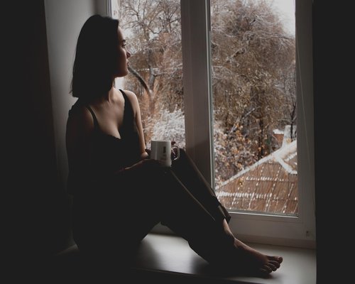 Person looking out of a window with a coffee mug